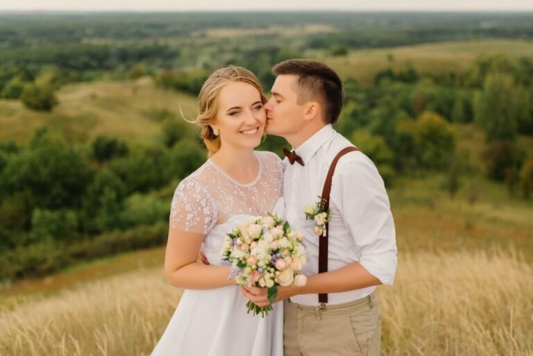 optimize-newlyweds-are-standing-against-beautiful-landscape-with-umbrella-groom-kisses-beautiful-bride-cheek.jpg